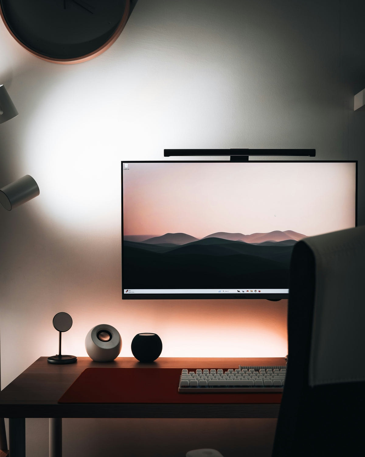 Monitor light bar clipped to top of a widescreen monitor on a minimal dark desk setup with warm ambient lighting