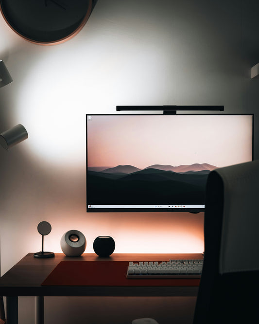 Monitor light bar clipped to top of a widescreen monitor on a minimal dark desk setup with warm ambient lighting